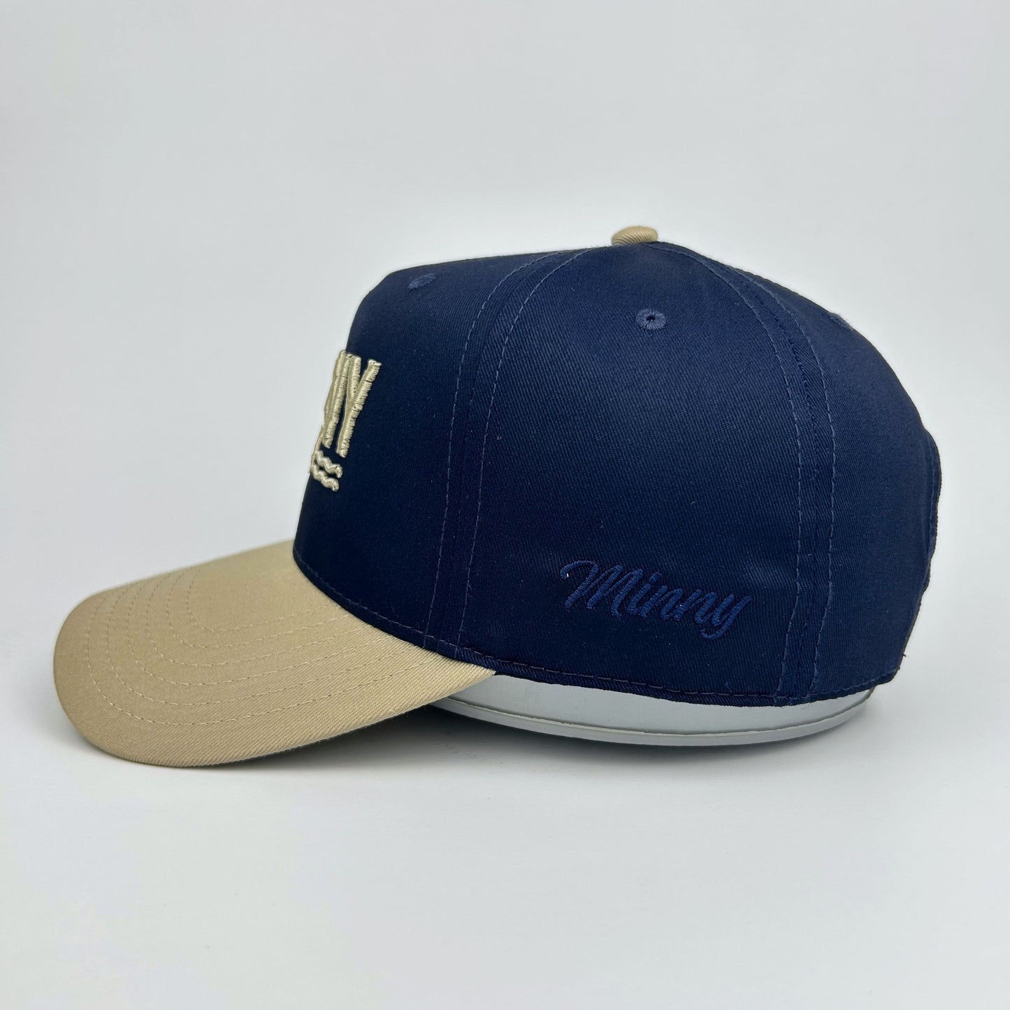 Navy and beige cap with 'Minny' branding on a light gray background