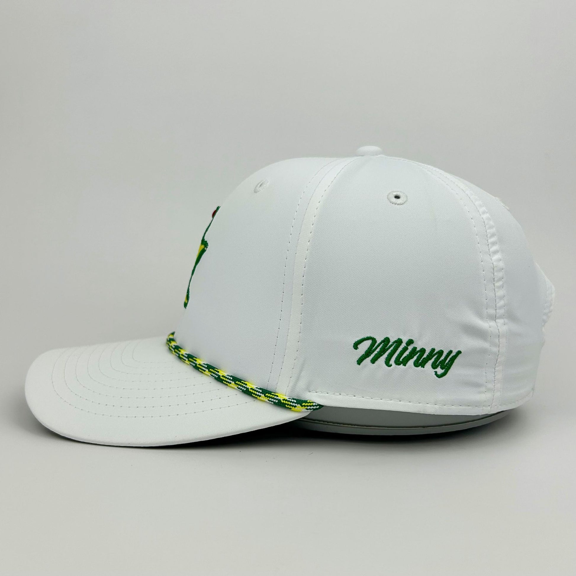 White cap with green text and braided band on a gray background