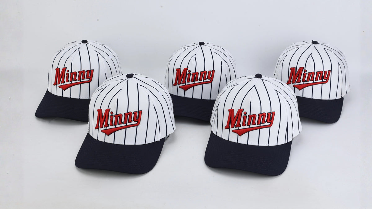 Five baseball caps with a white crown, thin navy pinstripes, and a dark navy brim, each featuring the word 'Minny' in red script with a white outline on the front. The caps are arranged on a plain light gray background.