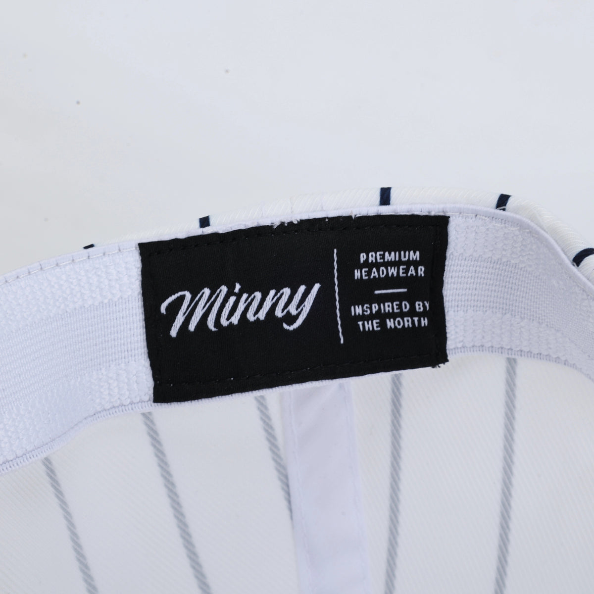 Close-up of a white pinstripe headband with a black brand label reading 'Minny Premium Headwear'.