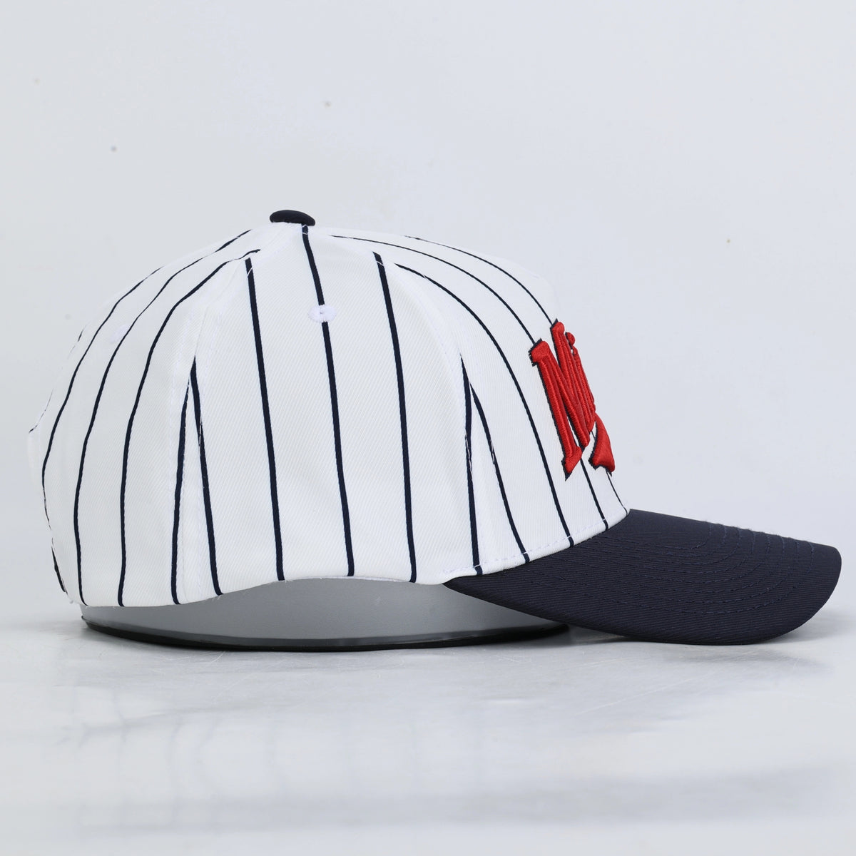A baseball cap featuring a white crown with thin navy pinstripes, a dark navy curved brim, and a red embroidered 'Minny' logo on the front.